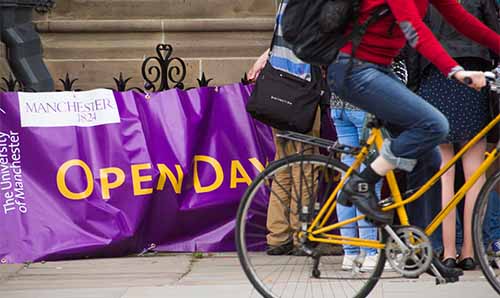 Cyclist going past open days sign