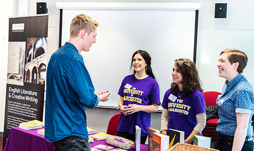 Man talking to two women at a stand promoting Creative Writing