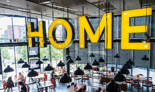 Big yellow letter sign hanging from ceiling in cafe that spells home