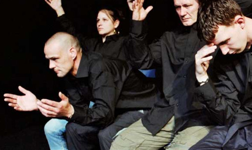 Four performers in black shirts gesturing with their hands out