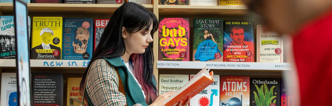 Female student pretending to read hardback next to book called Bad Gays