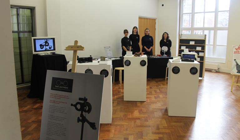 Photograph of the exhibition space and four students.