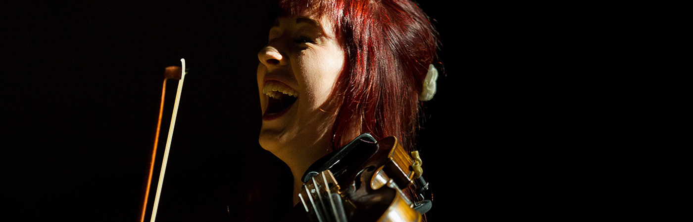 Female student playing the violin and laughing.