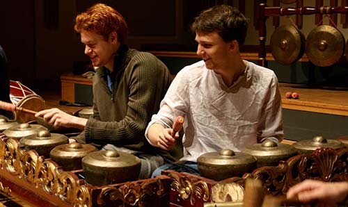 Two male students playing percussion instruments and smiling.