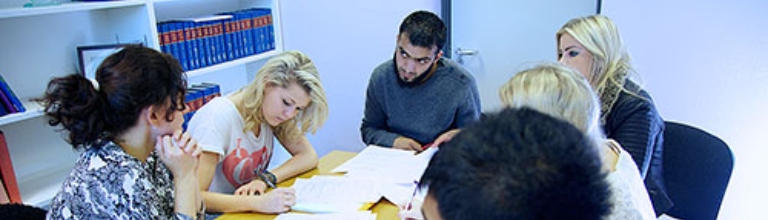 Students sat around table talking to staff with books on the shelf in the background