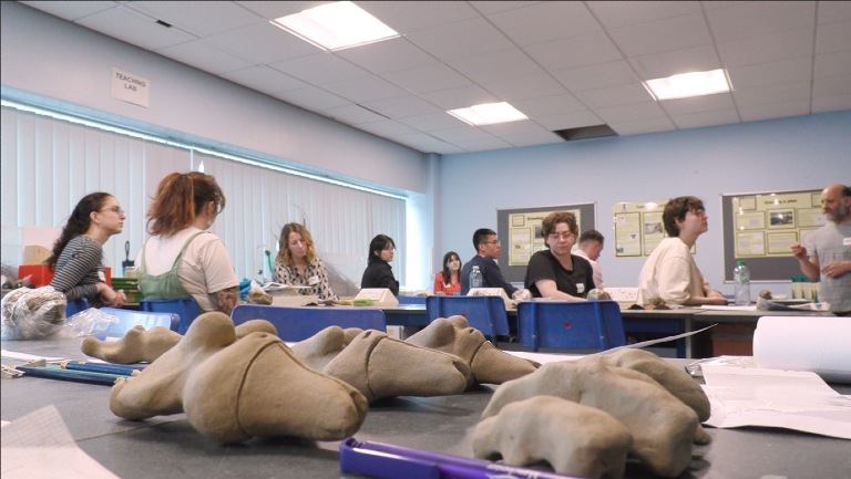 Clay figures on a table with a group of people in the background.