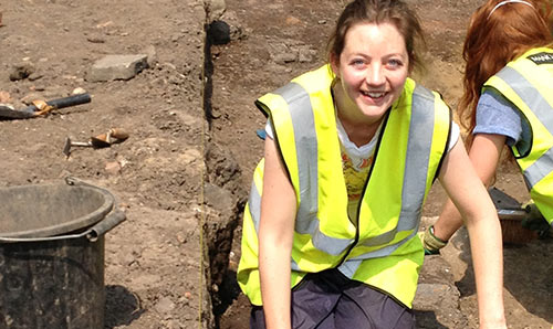 Female student smiling at camera during an archaeological dig.