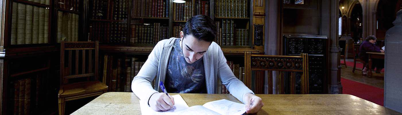 South Asian student writing in a dark John Rylands Library space