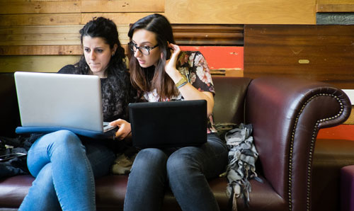 Two people sat down on sofa with laptops