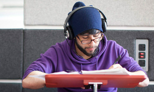 Man with headphones on sat down at table writing