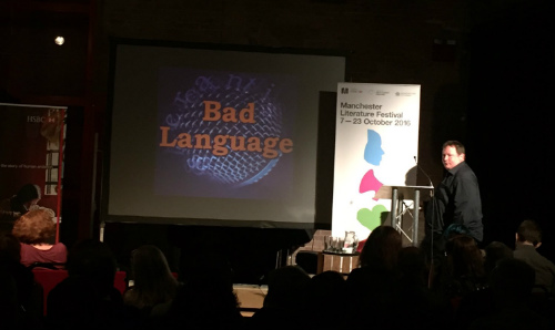 Event with people sat down and man on stage with Bad Language logo in the background