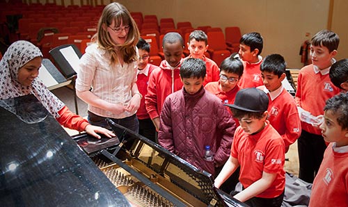 School children standing around a piano