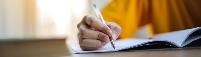 Close up of a person's hand  writing on a notepad with a pen. 