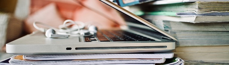silver laptop and white earbuds balanced on a stack of books