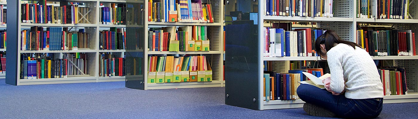 Female student sitting on floor reading a book in the library