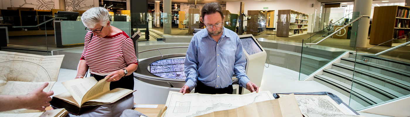 Members of research staff reading old maps in the library