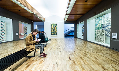 Girl sat on bench sketching in a gallery