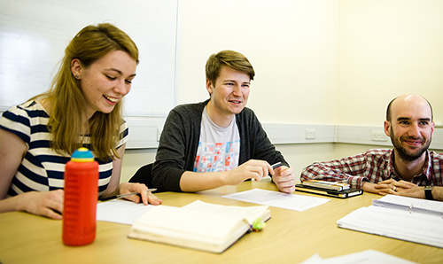 Three students sat at table laughing 