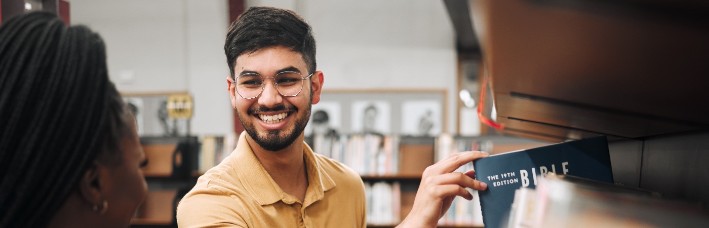 Male PGR student picking out a book in a library