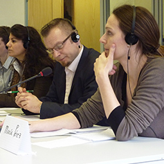 Three people sat behind desk with headphones on and microphone 