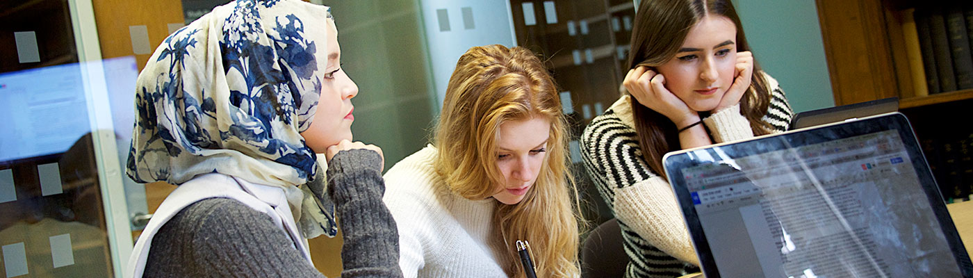 Three students sat at desk in front of laptop