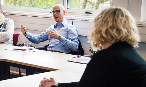 Male wearing glasses sat down talking with arms open