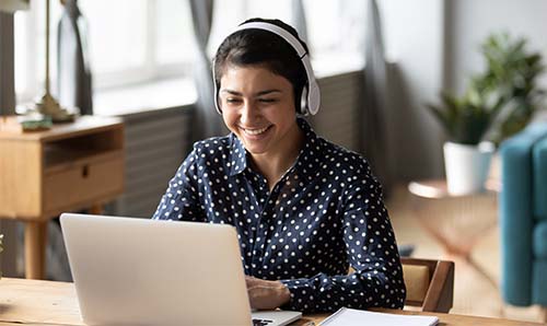 Female student working remotely on laptop and smiling.