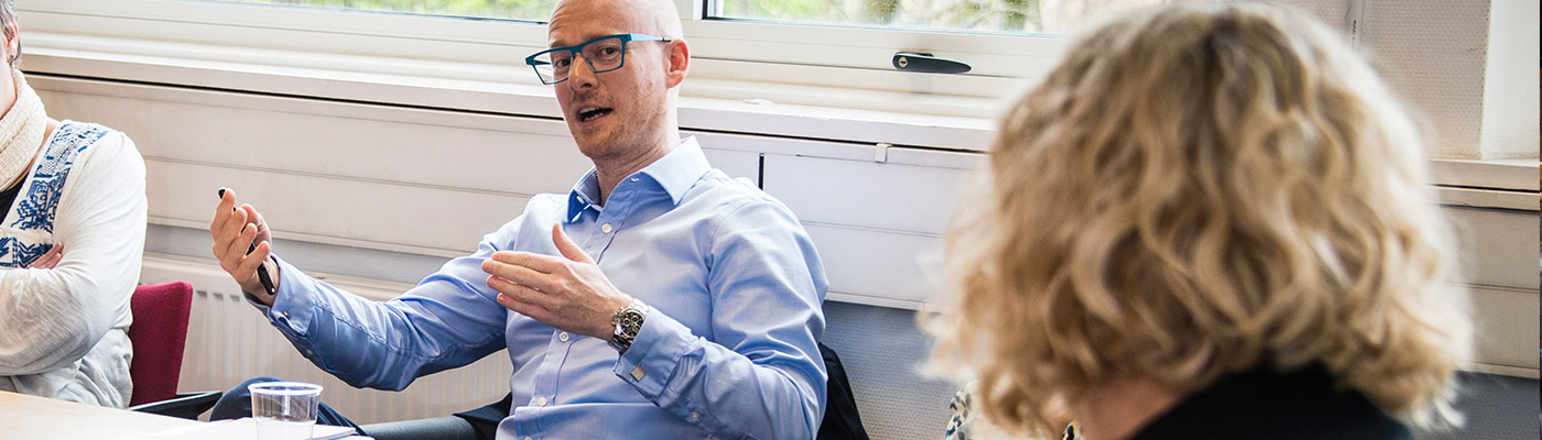 Male wearing glasses sat down talking with arms open