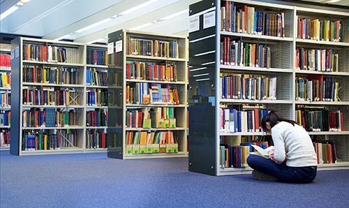 Female sat on the floor in library reading a book