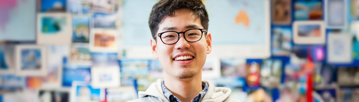 smiling student in front of travel noticeboard